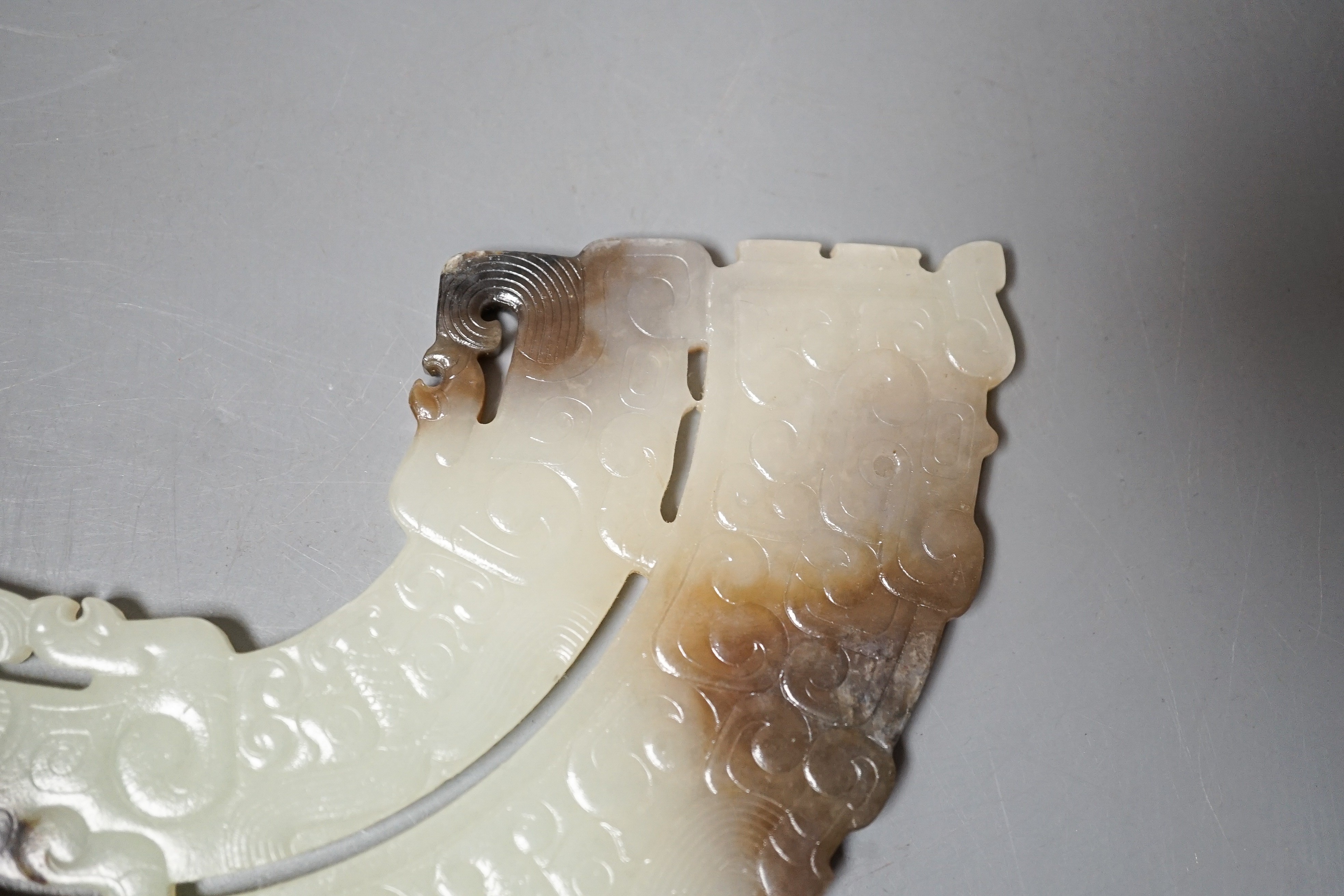 A Chinese archaistic jade fan shaped plaque, the pale celadon stone with brown and black inclusions, carved in low relief with taotie masks and leiwen, width 14.7cm